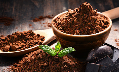 Composition with bowl of cocoa powder on wooden table