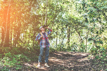 Naklejka na ściany i meble Young man with backpack and holding a binoculars looking in forest