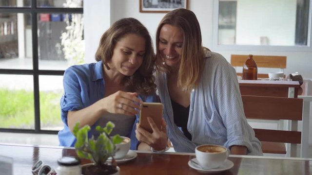 Two woman sharing coffee using smartphone in cafe