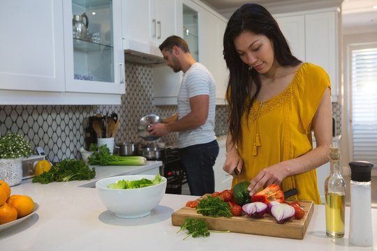 Woman Cutting Vegetables While Man Cooking Food In Kitchen