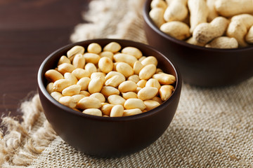 Peanuts in the shell and peeled close-up in cups. Roasted peanuts in their shells and peeled against a brown cloth.