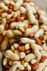 Peanuts in the shell and peeled close-up in cups. Roasted peanuts in their shells and peeled against a brown cloth.