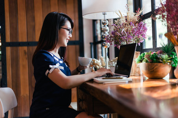 Asian business female hold a coffee mug working with laptop in coffee shop like the background.