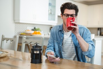 Man using mobile phone while having coffee in kitchen