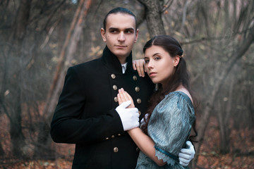 A man in a nineteenth century suit and a woman in a historical dress. Young man and woman in historical costumes in a gloomy forest