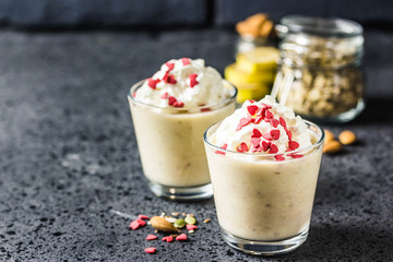 Festive banana almond milkshake with whipped cream sprinkled with hearts on dark background. Selective focus, space for text.