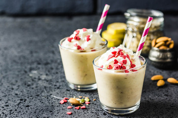 Festive banana almond milkshake with whipped cream sprinkled with hearts on dark background. Selective focus, space for text.