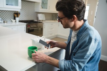 Man using mobile phone while having coffee in kitchen