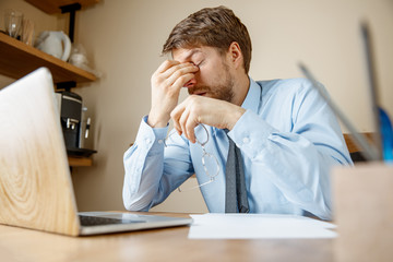 Feeling sick and tired. Frustrated sad unhappy sick young man massaging his head while sitting at...