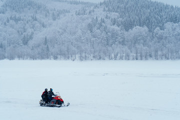 Fototapeta na wymiar Two man riding fast on a snowmobile in the snowy mountains near the forest