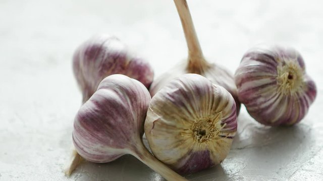 Closeup shot of composed pile of unpeeled garlic bulbs with stems lying on rough white surface in daylight
