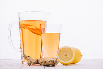 tea with lemon and ginger root in glass and jar on wooden table isolated on white