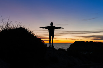 Sunset over the sea with silhouette of teenager with cap