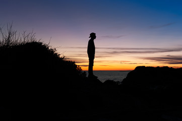 Sunset over the sea with silhouette of teenager with cap