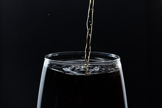 Glass of pouring fizzy drink with ice on a black background