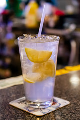 Alcohol drink on bar with lemon slices and a straw.  Blurred background.