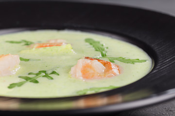 Close-up cream broccoli soup with shrimp in a beautiful black plate on a dark background. Seafood dish. Selective focus.