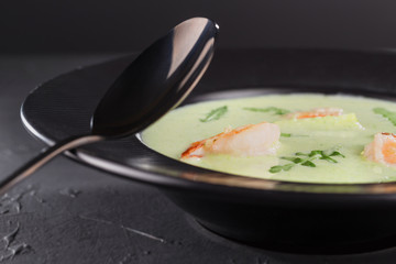Close-up cream broccoli soup with shrimp in a beautiful black plate on a dark background. Seafood dish. Selective focus.
