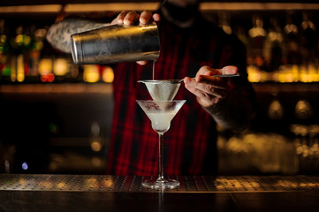 Bartender pouring fresh and sour drink into a cocktail glass