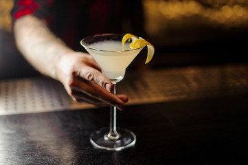 Barman holding a glass of fresh sour and sweet cocktail decorated with orange peel