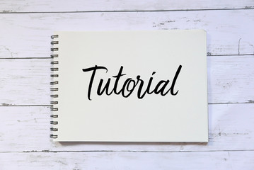Top view of notebook written with Tutorial on white wooden background.