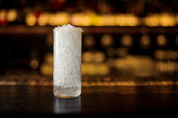 Cocktail glass with ice pieces on the bar counter in the background of golden lights