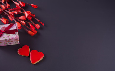 Valentines day concept with paper red flowers, two cookies hearts and gift box on black background.