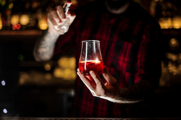 Tattooed barman sprinkling bitter into the glass with red sweet cocktail