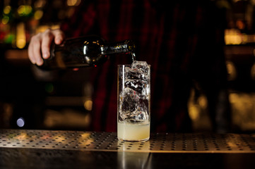 Barman pouring alcoholic drink from bottle into a cocktail glass with juice and ice