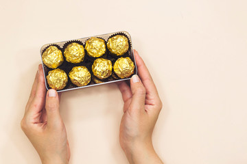 Fototapeta na wymiar closeup hand woman holding a box of golden premium chocolate sweets for valentine's or women's holiday