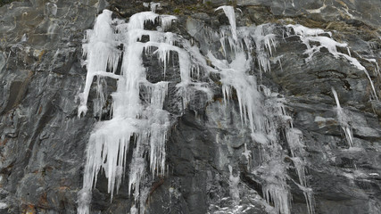 Fototapeta na wymiar Neve ghiacciata che pende dalla montagna, in ghiaccioli lunghi