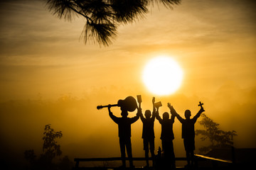 Youth christian group worship God by holding christian cross and guitars with light sun rise background,christian silhouette concept.