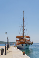 Big white brown wooden sailboat anchored next to the dock in town