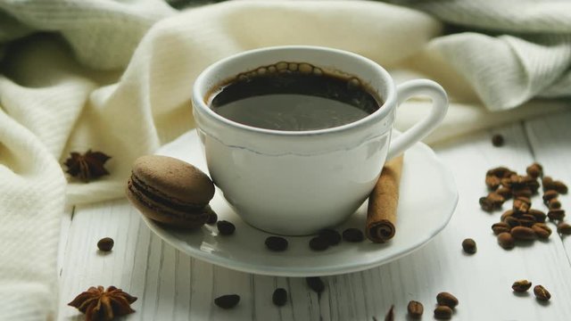 White elegant cup on saucer filled with black coffee and composed on white wooden table with spices