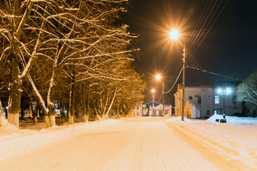 Winter night in a provincial northern Russian town: the road, tree branches under the snow, lanterns and buildings against the dark sky. Veliky Ustyug, Vologda Region, Russia.
