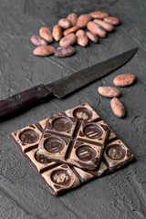 split chocolate tablet and group of cocoa beans on rustic black textured background