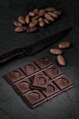 split chocolate tablet and group of cocoa beans on rustic black textured background
