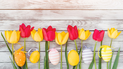 Easter eggs and tulips. Happy Easter card with copy space. Colorful easter eggs among fresh spring tulips. Decorated eggs on rustic wooden background. Easter holidays. Red and yellow spring tulips.