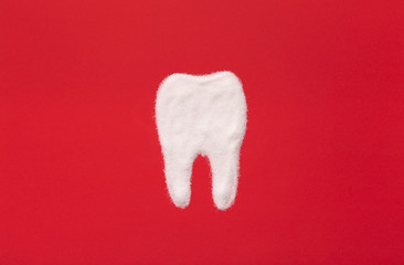 Tooth made from sugar on red background