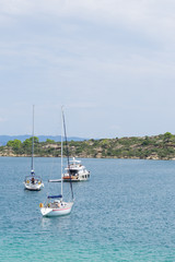 Fototapeta na wymiar Sailboats anchored near the seashore in front of the rocks and vegetation