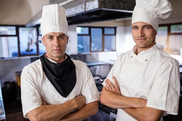 Two male chefs standing with arms crossed in kitchen