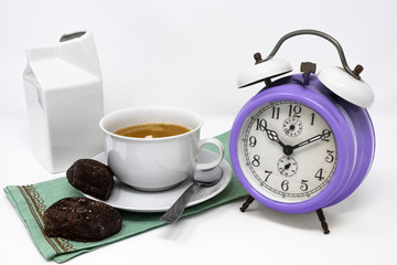 Traditional Italian breakfast with coffee and milk, cappuccino, and homemade chocolate biscuits. white ceramic cups on a white background. Vintage violet analog alarm clock. Wake up in the morning.