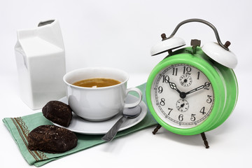 Traditional Italian breakfast with coffee and milk, cappuccino, and homemade chocolate biscuits. white ceramic cups on a white background. Vintage green analog alarm clock. Wake up in the morning.