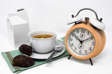 Traditional Italian breakfast with coffee and milk, cappuccino, and homemade chocolate biscuits. white ceramic cups on a white background. Vintage orange analog alarm clock. Wake up in the morning.