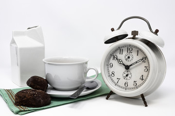 Fototapeta na wymiar Traditional Italian breakfast with coffee and milk, cappuccino, and homemade chocolate biscuits. white ceramic cups on a white background. Vintage white analog alarm clock. Wake up in the morning.