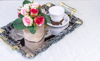 A tray with a white cup and flowers on a white cloth.