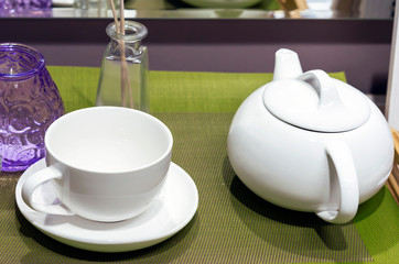 White ceramic teapot and cup on a green napkin.