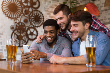 Diverse friends watching videos on smartphone and drinking beer