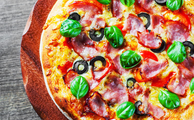 Pizza with Mozzarella cheese, ham, pepper, olive, meat, Tomato sauce, Spices and Fresh Basil. Italian pizza on wooden background