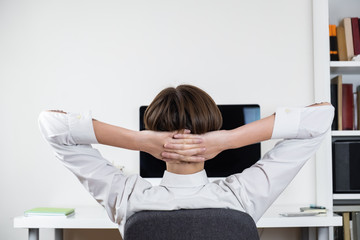 Procrastination concept: office worker stretching in front of black computer screen. Female employee sitting at desk and having rest at a workplace